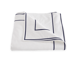 The Ansonia Bedding Collection by Matouk features a folded white Egyptian cotton percale bedsheet with a navy geometric border and satin stitching, shown against a plain background.