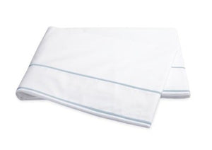 The Matouk Ansonia Bedding Collection in Blue features a soft cotton percale white bedsheet with two light blue edge stripes, neatly folded and displayed on a white background.