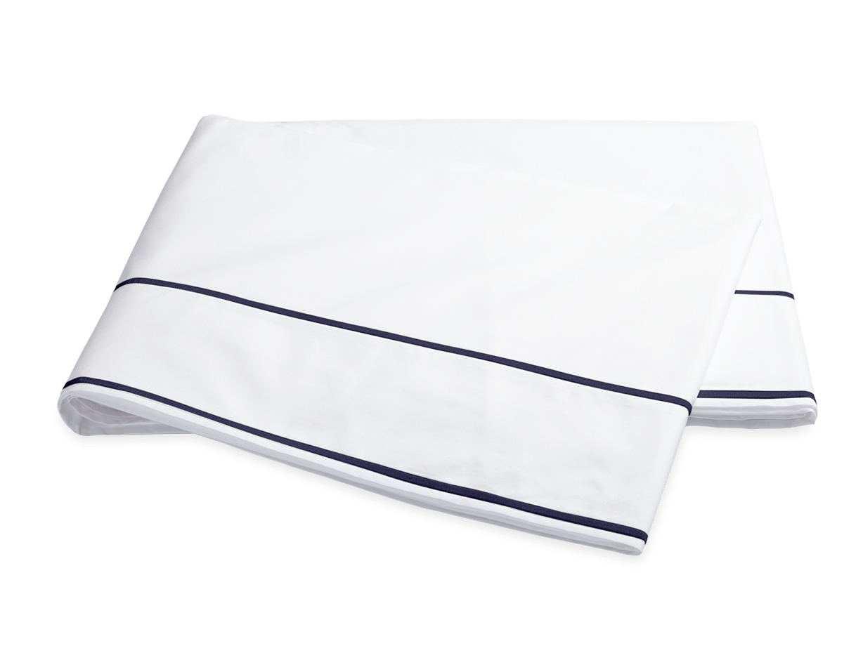 The Ansonia Bedding Collection by Matouk features a neatly folded white bedsheet with two thin navy blue stripes near the edge, crafted from luxurious 500 thread count Egyptian cotton percale.