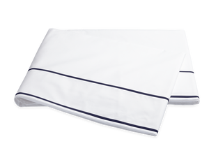 The Ansonia Bedding Collection by Matouk features a neatly folded white bedsheet with two thin navy blue stripes near the edge, crafted from luxurious 500 thread count Egyptian cotton percale.