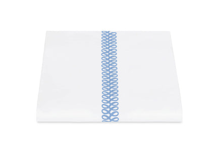 A neatly folded white sheet from Matouk’s Astor Braid Bedding Collection, Sky, crafted from Ceylon percale and featuring a single vertical blue embroidered Astor Braid down the center.