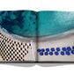 An Athens Riviera book by Assouline featuring an image of blue chairs on a beach.