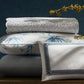 The Matouk Duma Diamond Bedding Collection in Navy, crafted from luxurious 500 thread count Egyptian cotton percale, features folded bedding and pillows with blue and white harlequin patterns on wood, with yellow flowers in the foreground.
