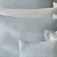 The Duma Diamond Bedding Collection, Sky by Matouk features white and light blue pillows and pillowcases with geometric patterns, embroidered scalloped edges, all crafted from luxurious Egyptian cotton for a refined touch.
