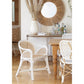The dining area showcases a wooden table with Selamat's Bolinas Dining Chairs featuring white rattan and cane weave detailing. Decorative vases enhance the decor as a mirror beautifully reflects light. A console table against the white wall displays assorted bottles and glassware for added elegance.