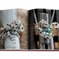 Displayed on an open page is a captivating image of two intricately designed, jeweled rings shaped like animals, encapsulating modern femininity with their exquisite gemstones and diamonds. The scene is set against a metallic industrial backdrop, with one design capturing the elegance of the iconic Cartier Panthere by Assouline.