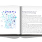 An open book displaying text on the right page and an illustration with the word "Comporta Bliss" in blue letters on the left page. The illustration includes people, animals, and various objects, reflecting the vibrant artistic community and nearby beaches of Comporta. The book is by Assouline.