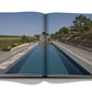 Open book displaying a photograph of a peaceful, rectangular swimming pool with wooden decking, surrounded by greenery and distant buildings under a clear blue sky—reminiscent of the serene beaches of Comporta Bliss, celebrated by its artistic community—by Assouline.