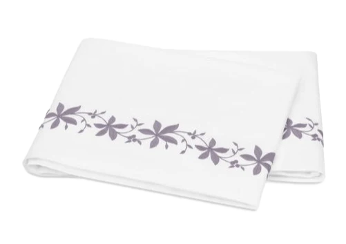 A folded white bed sheet from the Matouk Callista Bedding Collection, Lilac, features lilac floral embroidery along one edge and is crafted from luxurious Giza Egyptian cotton.