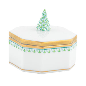 The Herend Christmas Tree Box, Green Multicolor, features a white hexagonal porcelain shape with gold trim, green hand-painted designs, and a lid topped by a sculpted pine tree.