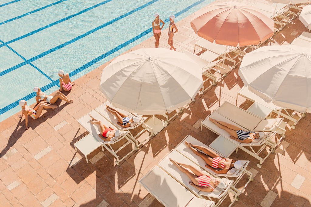 People enjoying poolside glamour on sun loungers by a swimming pool under parasols at the Gray Malin Coral Casino Beach & Cabana Club, White Frame, 15.5” X 21”.