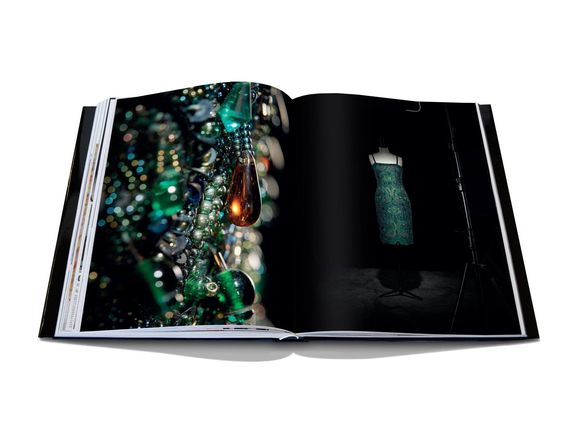 An open fashion book displays a page showcasing colorful jewelry and another featuring a green dress on a mannequin, reminiscent of haute couture designs by Dior IV by Gianfranco Ferré from Assouline.