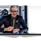 A man in glasses and a dark suit adjusts his sleeve while smiling in an open book spread, exuding luxury against a minimalistic background, featuring Diamonds: Diamond Stories by Assouline.