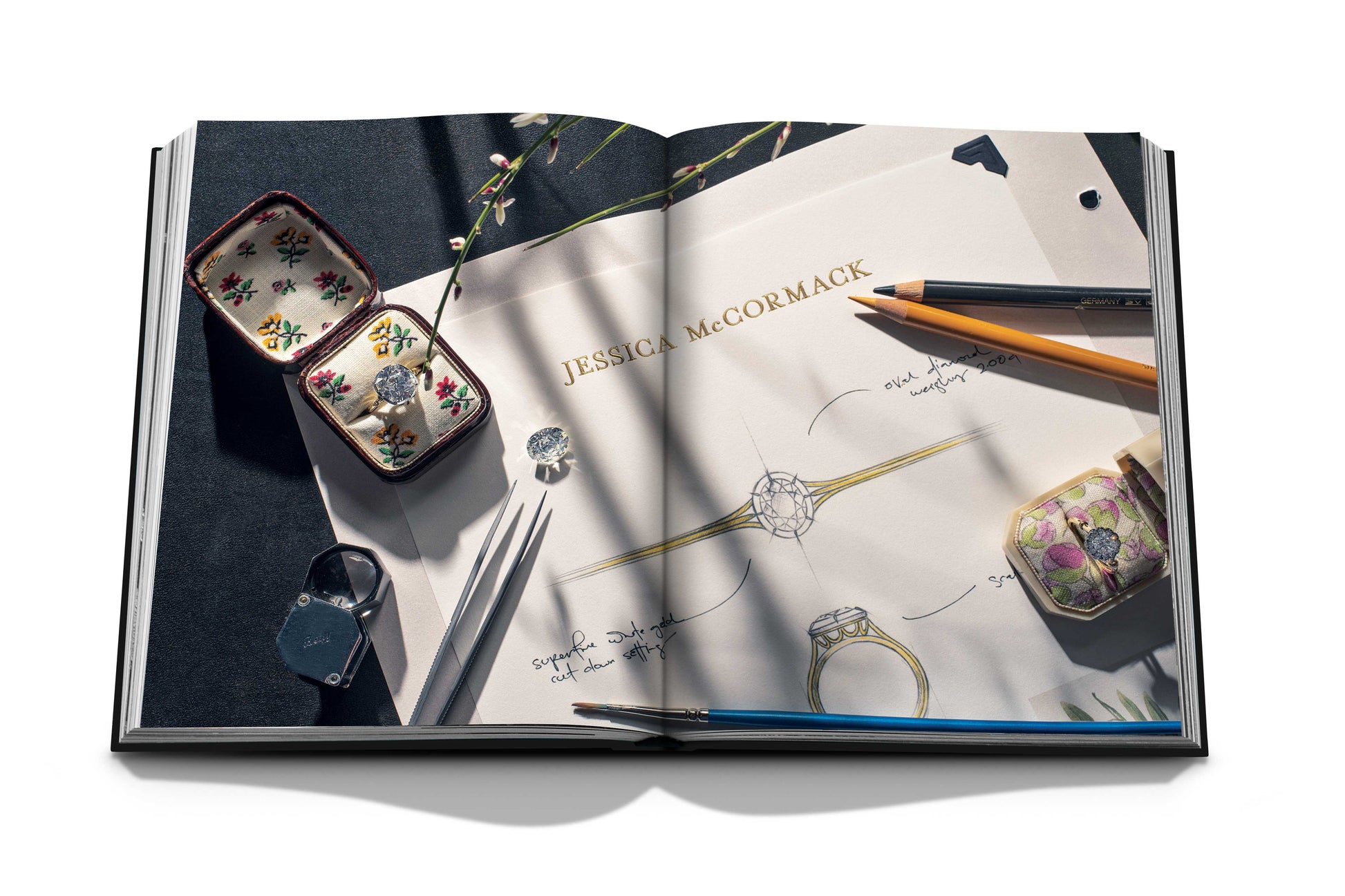 Open book showing jewelry design sketches, pencils, and ornate ring boxes. The design paper features a "Diamonds: Diamond Stories" heading, along with detailed ring illustrations and notes, embodying the elegance expected from luxury jewelry houses specializing in natural diamonds by Assouline.