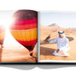 An open book from Assouline's "Dubai Wonder" displays vibrant hot air balloons over a desert on one page and a person in traditional attire with a falcon on the other, celebrating the cultural diversity often highlighted in Dubai tours.