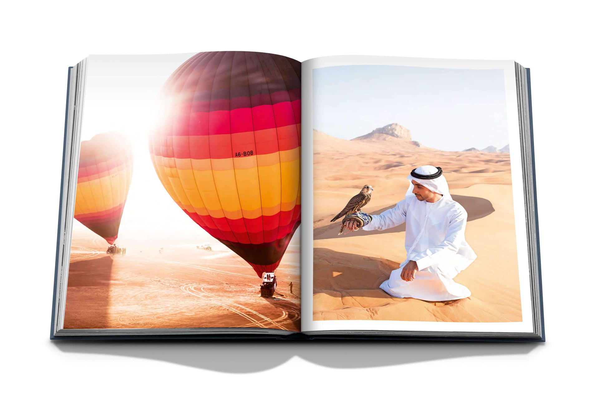 An open book from Assouline's "Dubai Wonder" displays vibrant hot air balloons over a desert on one page and a person in traditional attire with a falcon on the other, celebrating the cultural diversity often highlighted in Dubai tours.
