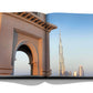 An open book, "Dubai Wonder" by Assouline, displays a photo of Dubai's skyline featuring the Burj Khalifa and an intricately designed archway under a clear blue sky, capturing the essence of cultural diversity in Dubai tours.