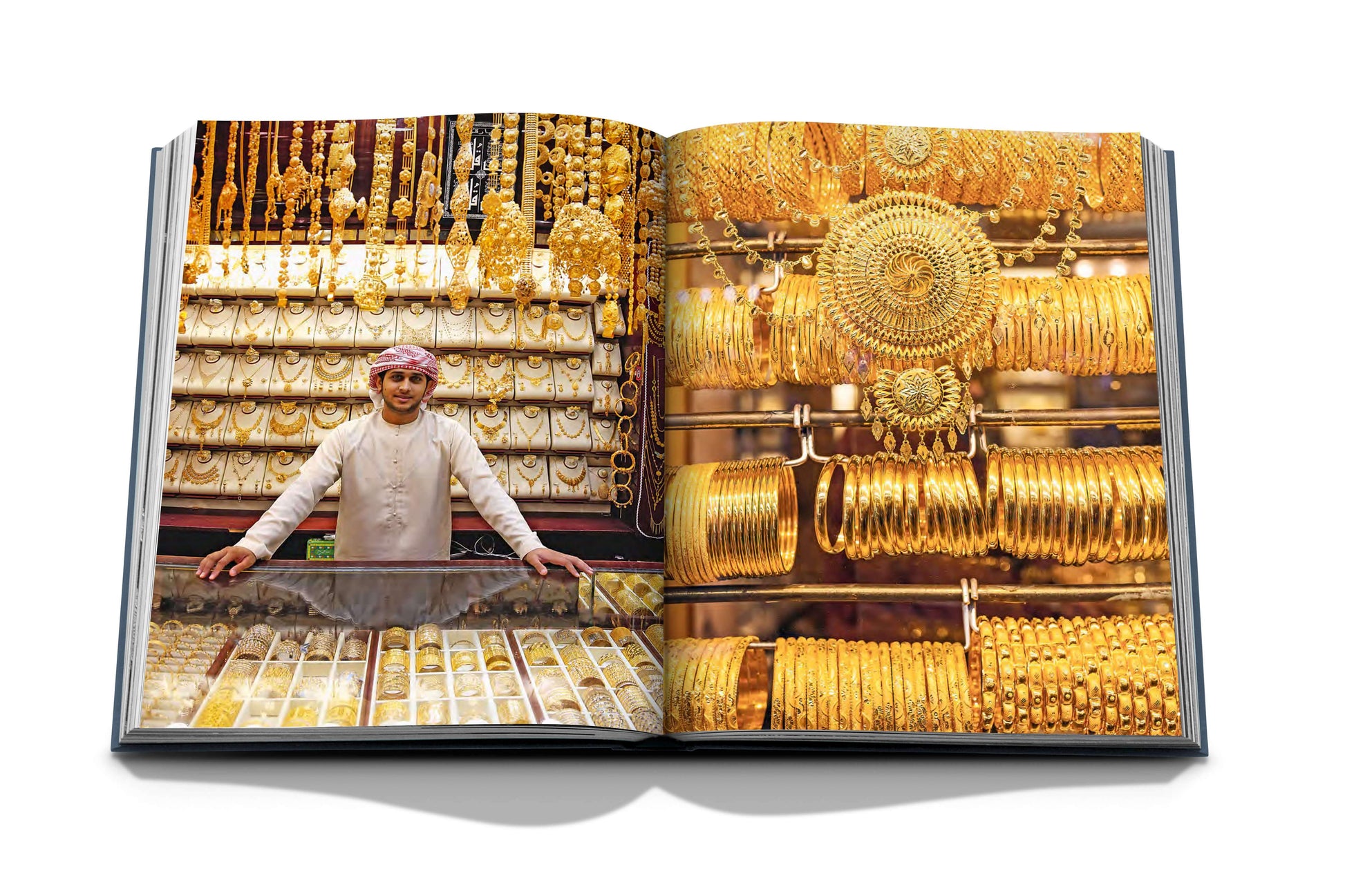 Open book featuring "Dubai Wonder" by Assouline: gold jewelry on the left page, with various bangles and ornaments on the right. A person behind the counter highlights Dubai's rich cultural craftsmanship, akin to a snapshot from diverse tours in Dubai.