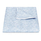 The Duma Diamond Bedding Collection in Sky by Matouk, made from OEKO-TEX® certified cotton, features a blue and white geometric pattern blanket neatly folded with one corner flipped on a white background.