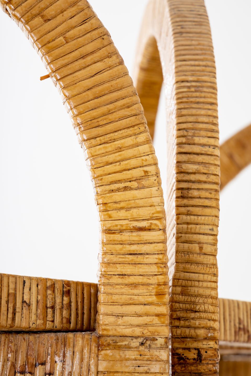 Close-up of a beige handle on the Florida-Style Rattan Etagere by HIVE Home, Gift, and Garden, featuring a textured, woven pattern and illuminated by natural light against a white background, reminiscent of the Palm Beach coastal style.