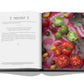 Open cookbook, titled "Chateau Life" by Assouline, displaying a recipe for simple tomato and basil sauce on the left page, with various ripe tomatoes and basil leaves artfully arranged on a colorful tablecloth on the right page, evoking rich culinary traditions.