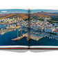 Opened Assouline travel book displaying a panoramic view of Tinos, one of the Greek Islands in the Aegean Sea, Greece.