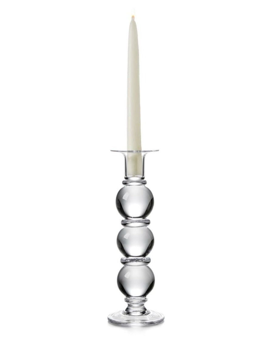 A tall white taper candle sits in the Simon Pearce Hartland Large Candlestick, featuring three glass spheres, handcrafted by artisans and shown against a white background.