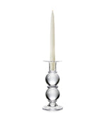 A white taper candle sits in the Simon Pearce Hartland Medium Candlestick, handmade by expert glassblowers with two round sections, shown against a plain white background.