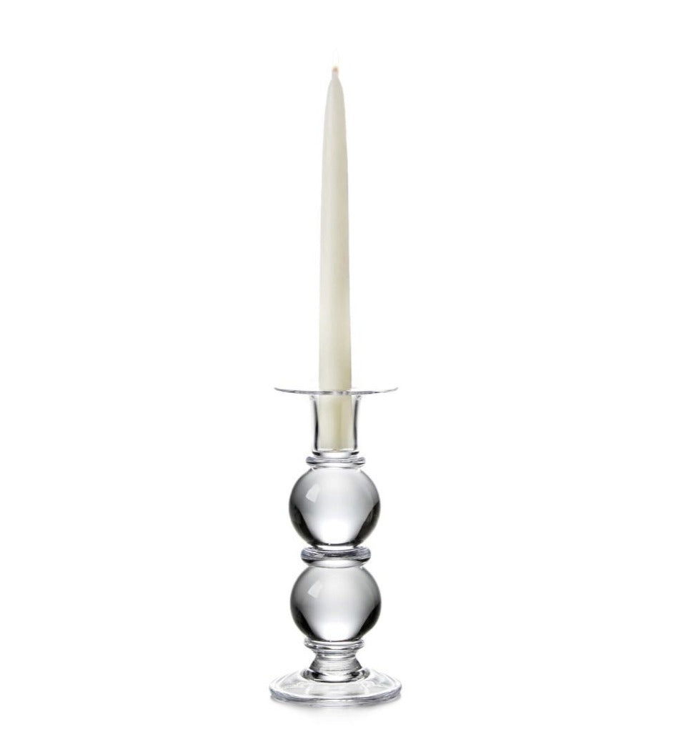 A white taper candle sits in the Simon Pearce Hartland Medium Candlestick, handmade by expert glassblowers with two round sections, shown against a plain white background.