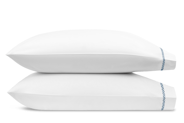 Two Matouk Hatch Navy pillows with French knot stitching stacked on top of each other against a light green background.