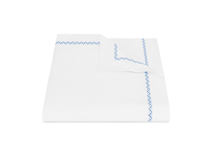 The Matouk Hatch Bedding Collection, Sky, features a white bedsheet and pillowcase set with blue zigzag and French knot stitching on the edges, crafted from luxurious 520 thread count Ceylon percale and displayed on a plain background.