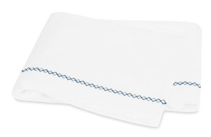 White towel with blue Matouk Hatch Bedding Collection Navy stitching embroidered edge folded on a plain background.