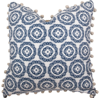 A handmade 22" x 22" pillow featuring a white background and a repeating blue circular pattern, adorned with beige pom-poms along the edges, the Tassel Inverted Medallion Navy Pillow by Associated Design.