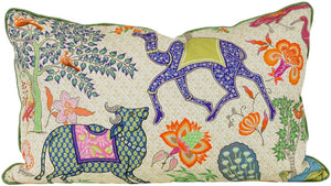 The Le Jardin De Exotiq Pillow by Hive Custom Pillows is a handmade rectangular piece featuring colorful, intricate illustrations of a camel, sheep, birds, and floral patterns on a light background with green trim. Made in the USA, it adds an artistic touch to any space.