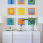 The Modern 6122 sideboard by Ornis Gallery, styled with a vase, glassware tray, and books, sits beneath nine framed geometric abstraction artworks printed on archival paper in custom colors. Two lamps flank the sideboard on a white wall.