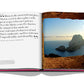 Open book on a desk showing a quote about Ibiza Bohemia and a full-page photograph of Balearic cliffs in the sea at sunset by Assouline.