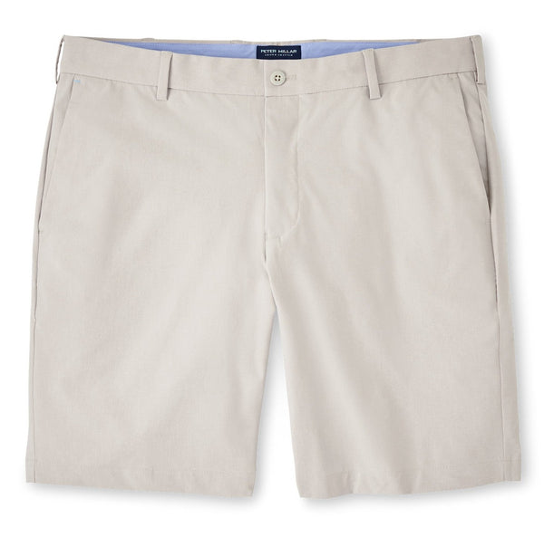 A pair of Peter Millar Surge Performance Shorts for men in beige with a flat front and a visible blue waistband lining displayed on a white background.