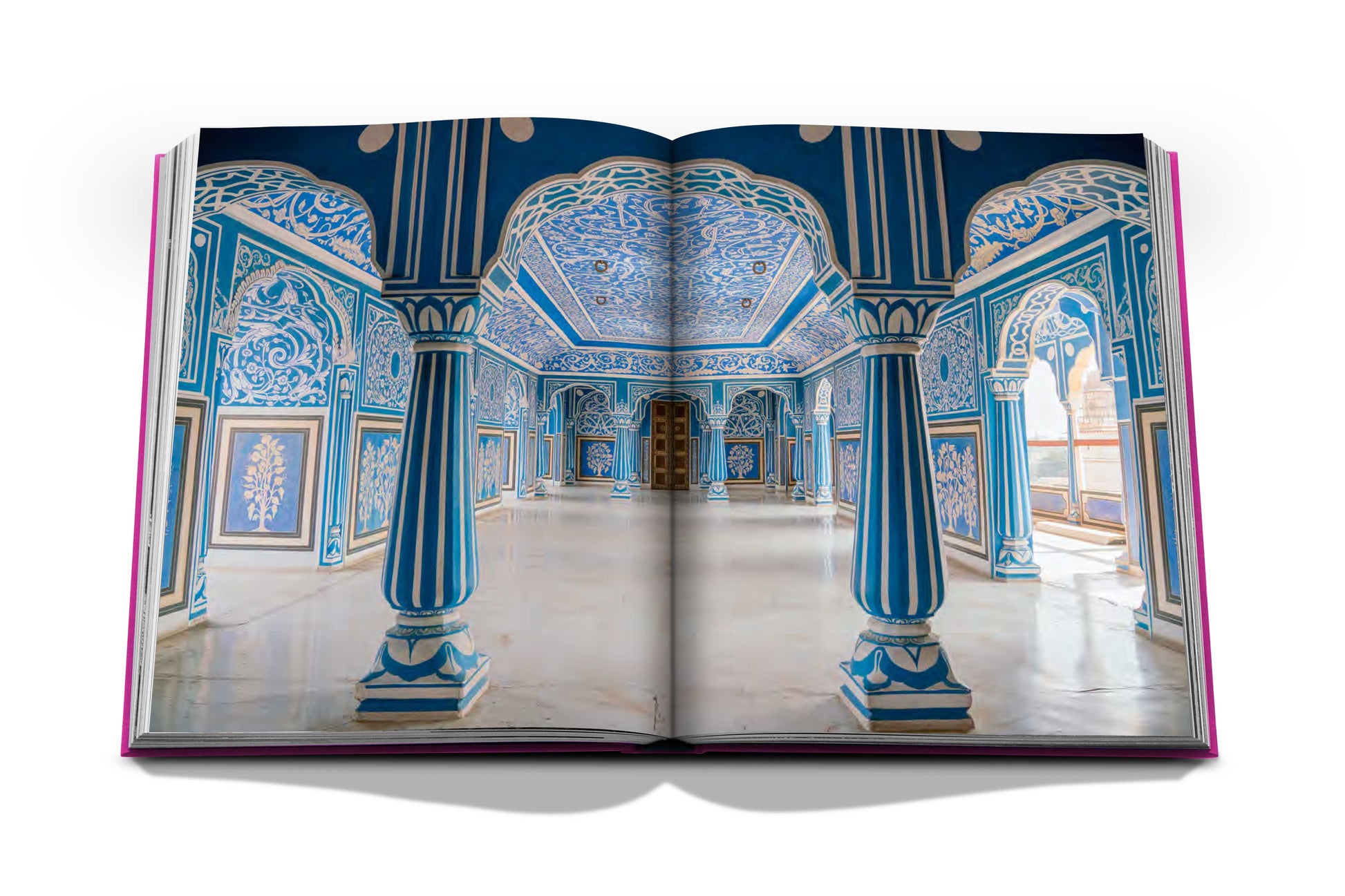 An open book displaying a page with an elaborately decorated hall reminiscent of Jaipur's architectural grandeur, featuring blue and white intricate designs, columns, and archways from the Jaipur Splendor by Assouline.