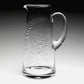 The William Yeoward Crystal Jasmine 4 Pint Pitcher features clear glass with a handle, spout, and engraved leafy branch design, displayed against a gradient background.