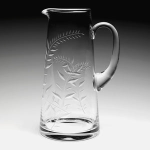 The William Yeoward Crystal Jasmine 4 Pint Pitcher features clear glass with a handle, spout, and engraved leafy branch design, displayed against a gradient background.