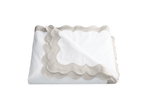 The Lorelei Bedding Collection in Silver by Matouk features a neatly folded white sheet with a light gray scalloped border, styled on a plain background for an artisanal look.