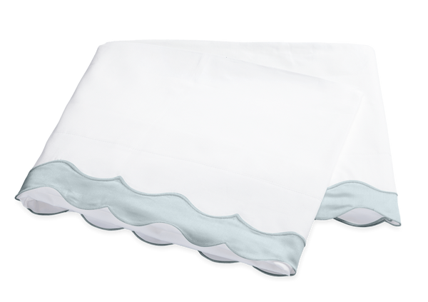 Two folded Matouk Lorelei Pool towels with wavy light blue applique scallop trim on a black background.