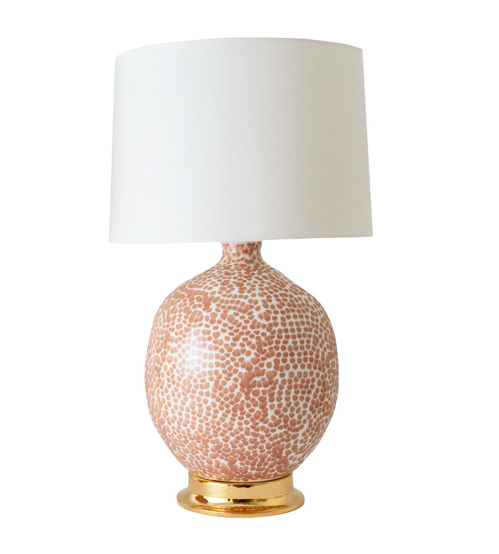 The Marfa Round Dappled Coral Lamp by Paul Schneider Ceramics features a ceramic gold base, solid brass dimmer socket, and a plain white cylindrical shade.