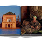 An open book displaying two photographs: on the left, a building beside a body of water with mountains in the background reflecting Marrakech Flair arts; on the right, a woman in a patterned dress. (Assouline)