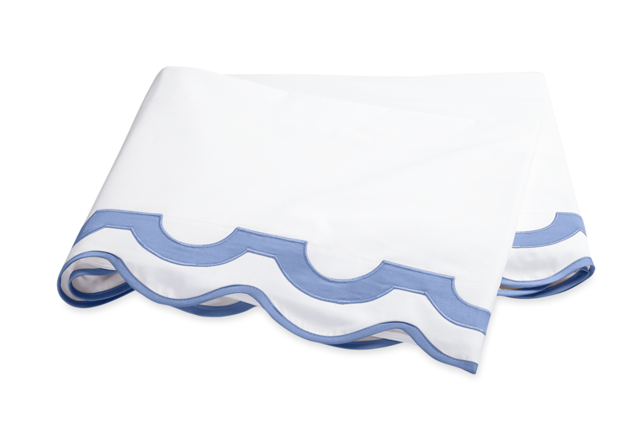 A folded white bedsheet with a light blue scalloped edge, crafted from 600 thread count Egyptian cotton percale—an elegant piece from the Matouk Mirasol Bedding Collection, Azure.