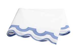 A folded white bedsheet with a light blue scalloped edge, crafted from 600 thread count Egyptian cotton percale—an elegant piece from the Matouk Mirasol Bedding Collection, Azure.