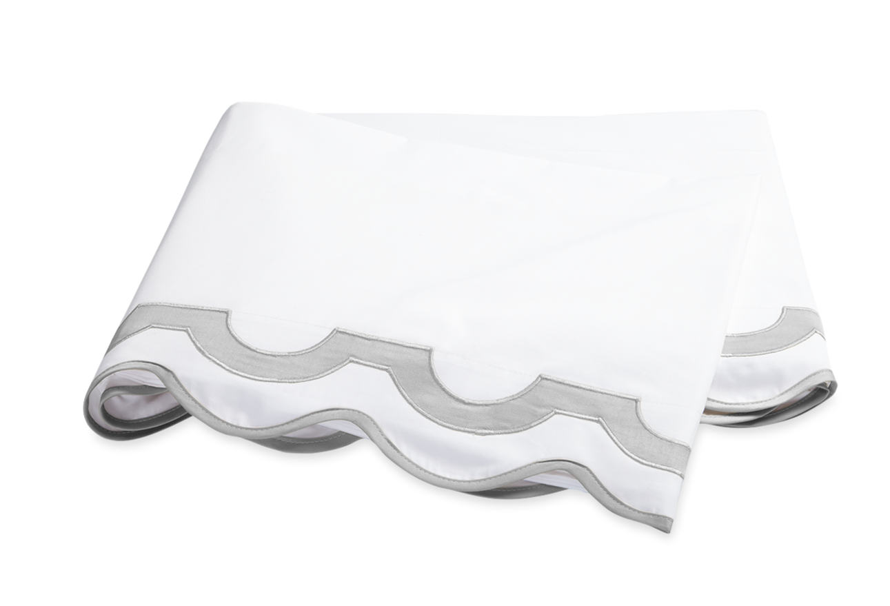 The Mirasol Bedding Collection in Silver by Matouk features a folded white bedsheet with a gray scalloped border, crafted from Egyptian cotton percale with a 600 thread count, displayed on a white background.