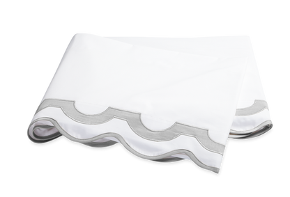 The Mirasol Bedding Collection in Silver by Matouk features a folded white bedsheet with a gray scalloped border, crafted from Egyptian cotton percale with a 600 thread count, displayed on a white background.