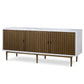 The Naples Cabinet by Mr Brown is a modern wooden sideboard with a sleek white frame. It features four vertically grooved doors finished in smooth white gesso and is raised on slim legs.
