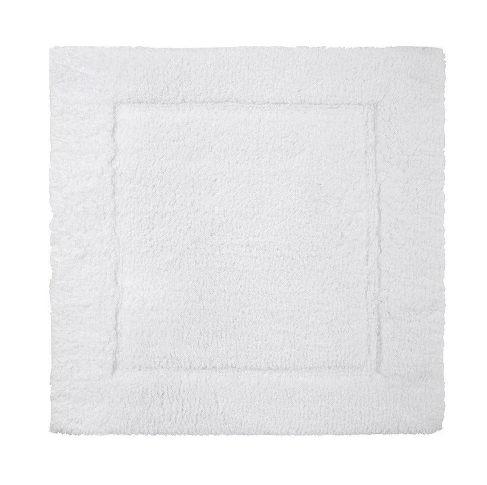 The Yves Delorme Prestige Blanc Bath Mat is a white rectangular mat with a subtle raised border, crafted from 100% cotton for plush comfort, shown from above on a plain background.